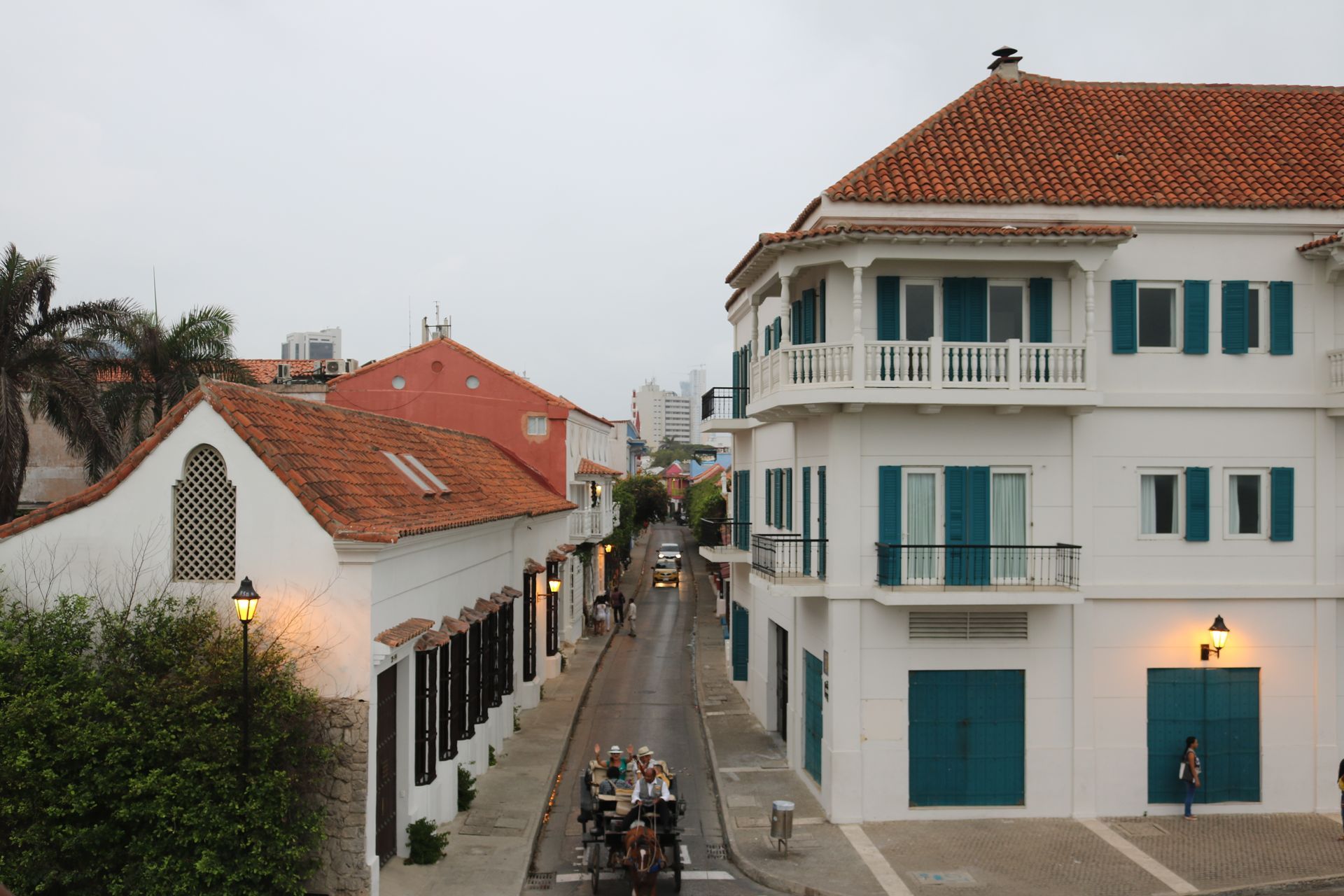 Narrow canal street between white and red-roofed buildings at dusk, with a few cyclists below