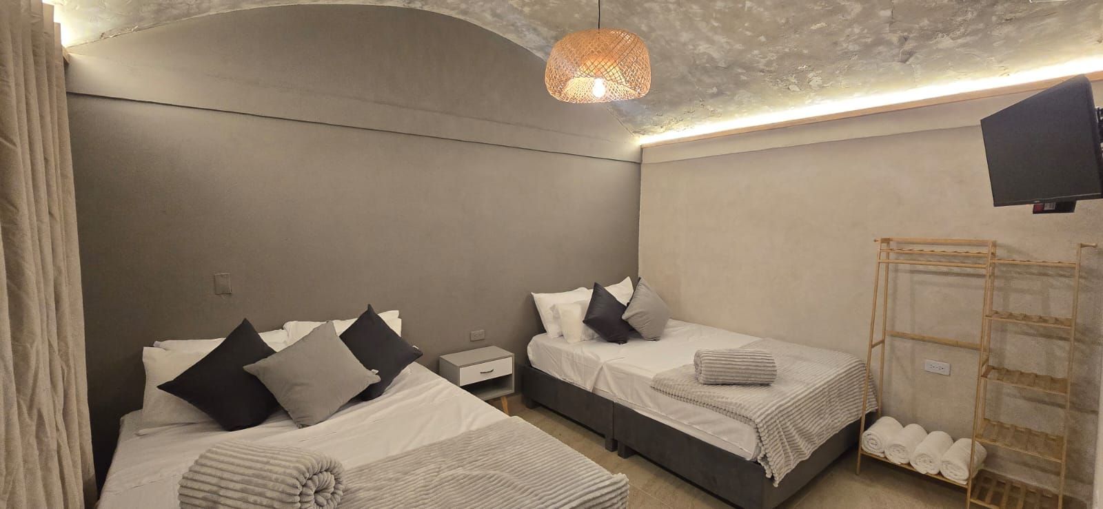 Cozy bedroom with two twin beds, soft lighting, and a wicker shelf in a beige room