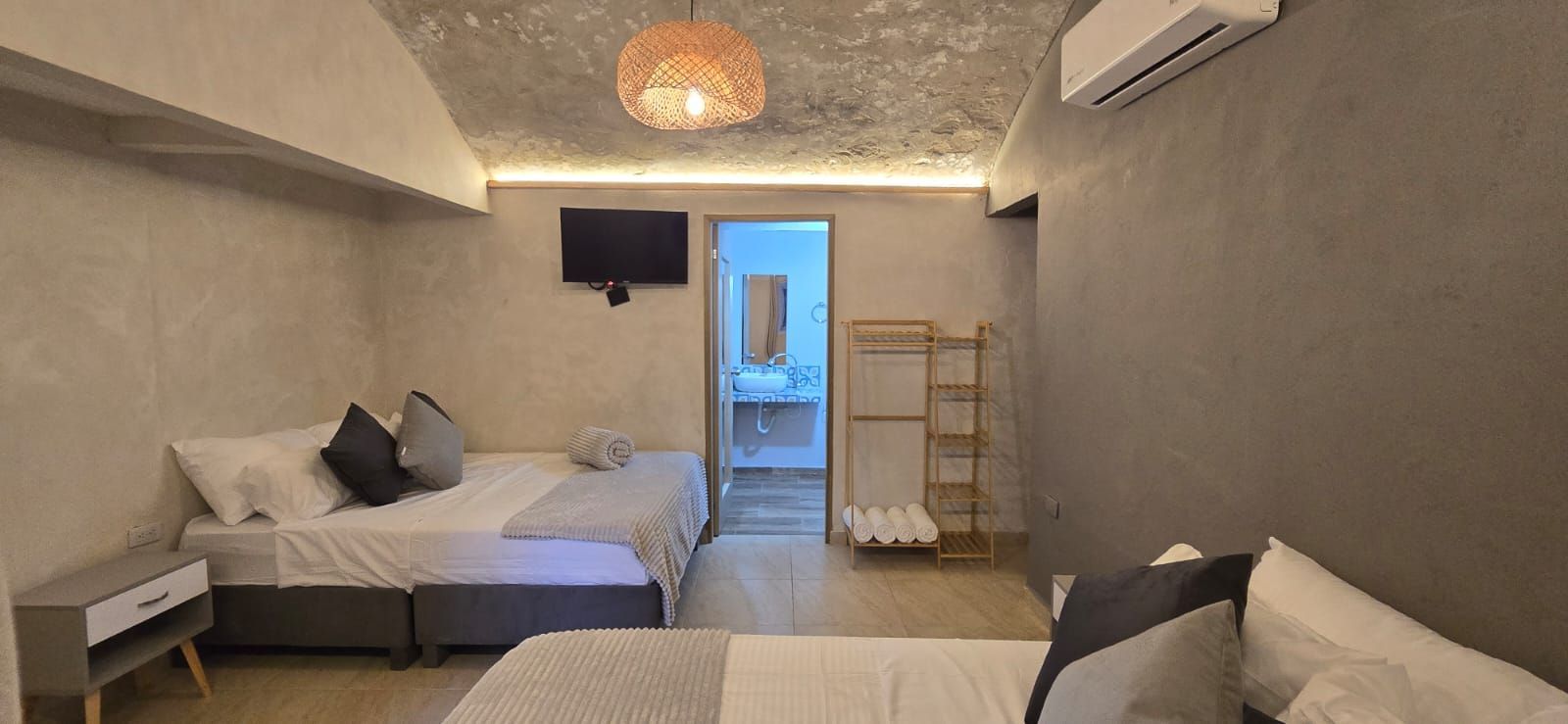 Hotel room with two beds, brick walls, desk, TV, and decorative plants.