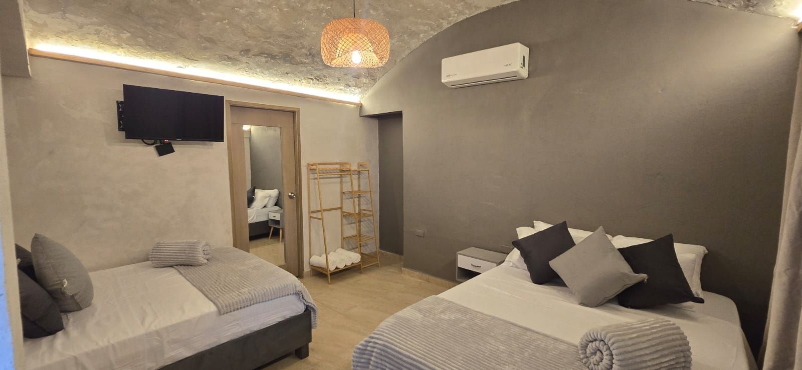 Modern bedroom with two beds, gray walls, wall-mounted TV, mirror, and warm ceiling light