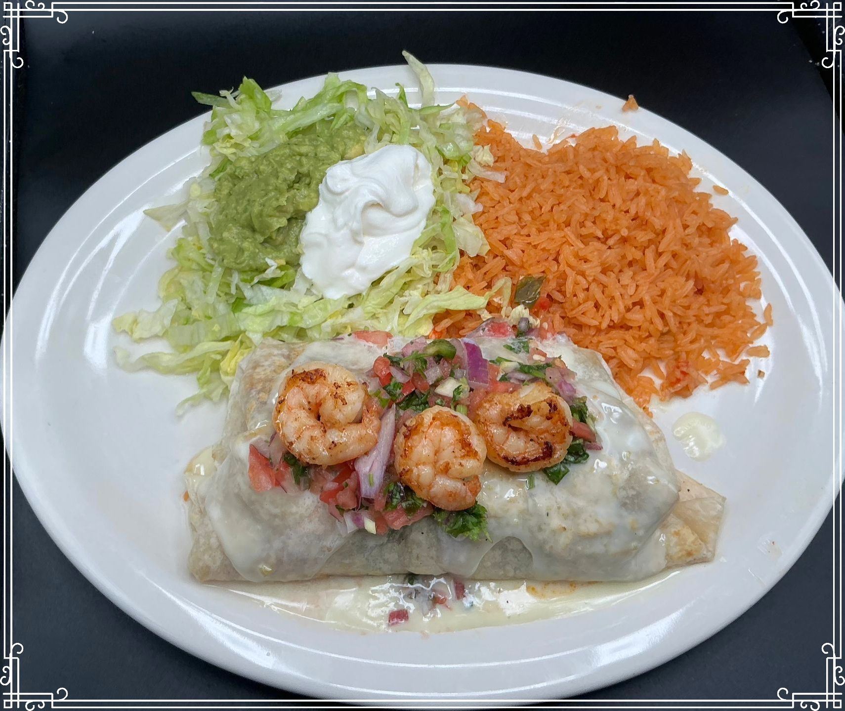 Burrito with shrimp, rice, lettuce, guacamole, and sour cream on a white plate.