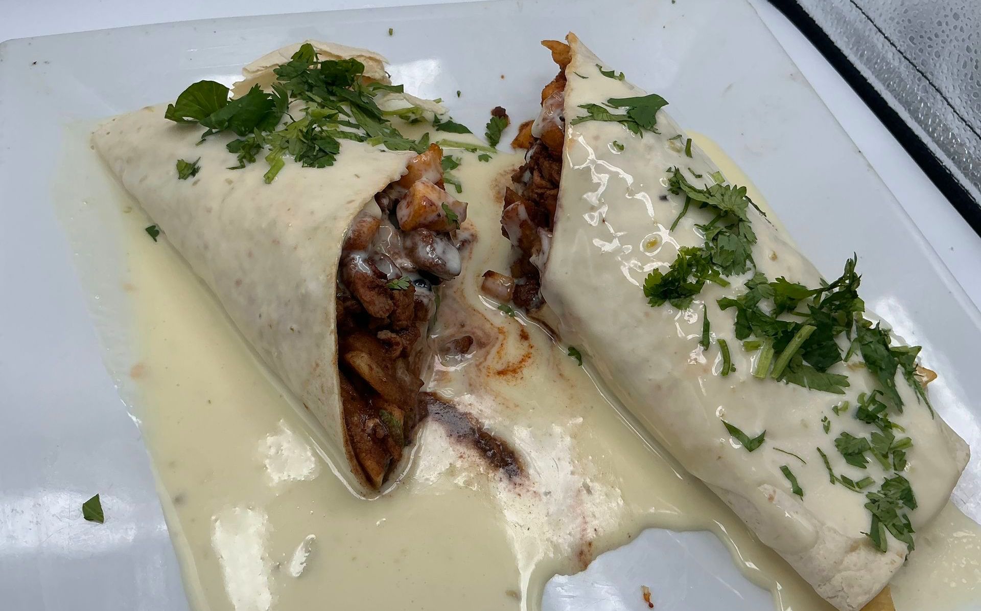 Two burritos covered in creamy sauce and cilantro, cut open, on a white plate.