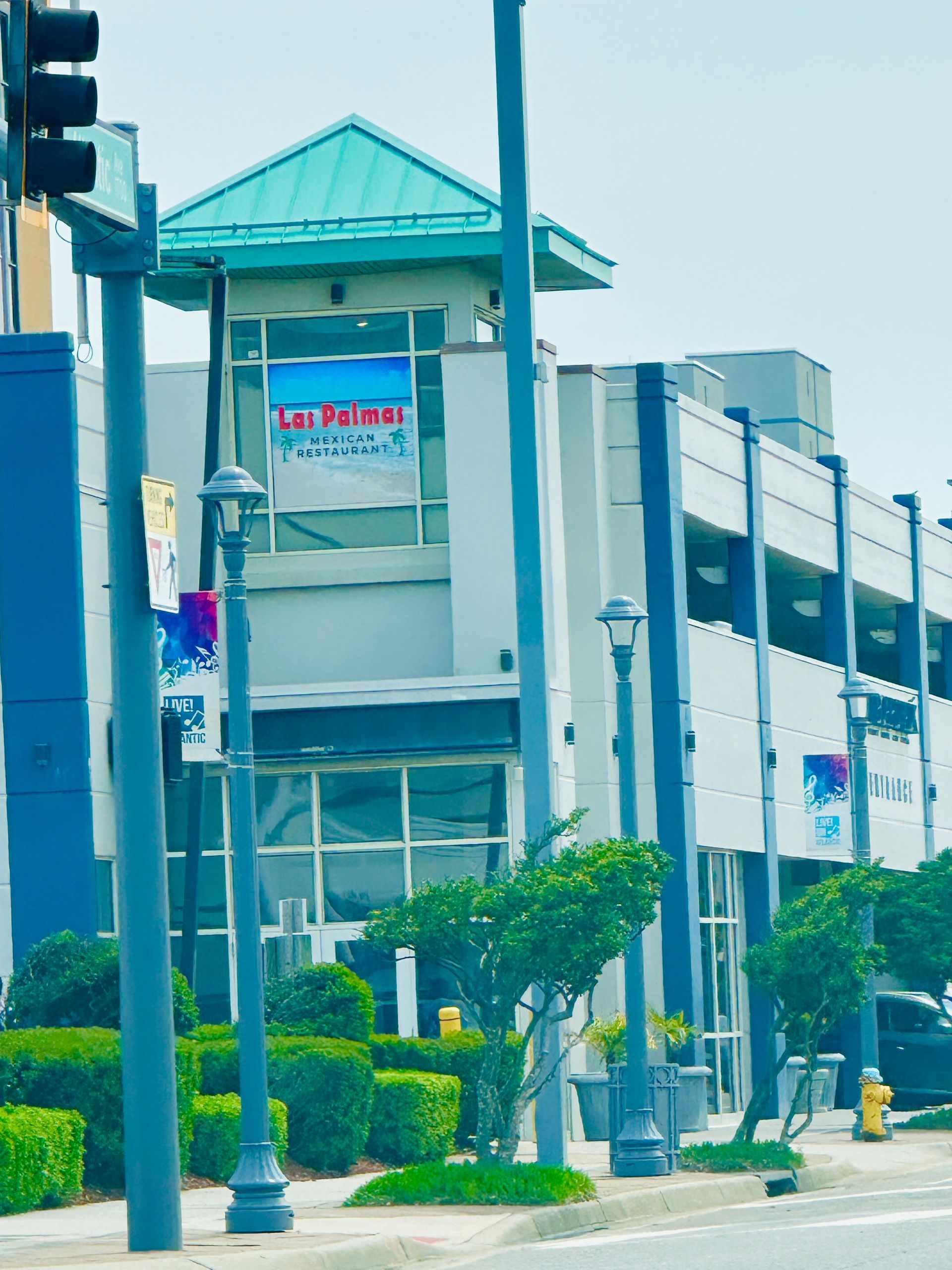 Building with blue and white facade, teal roof, and storefronts. Signs on the windows and sidewalks in front.