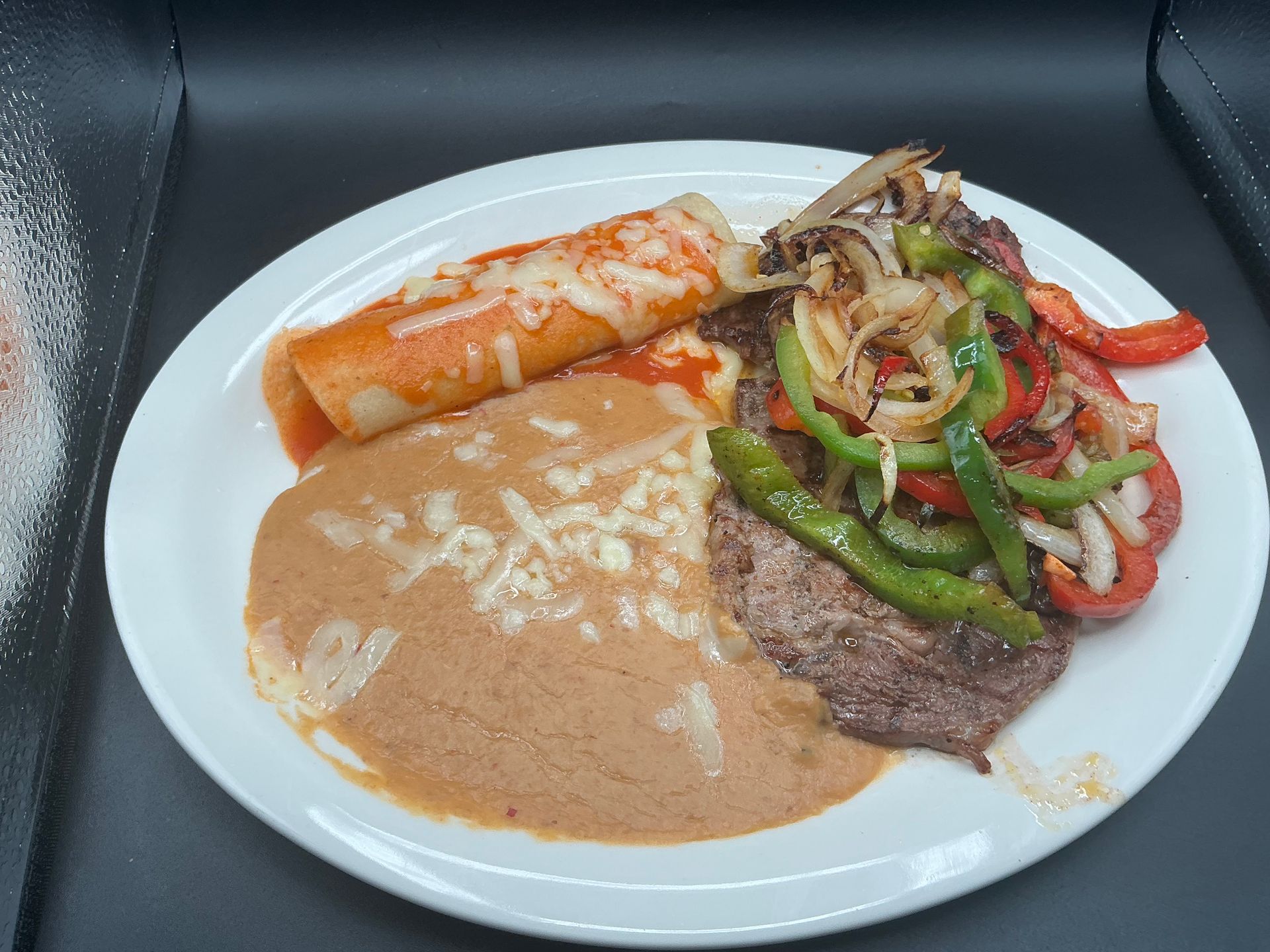 Plate of Mexican food: enchilada, meat, sauteed peppers and onions, refried beans.