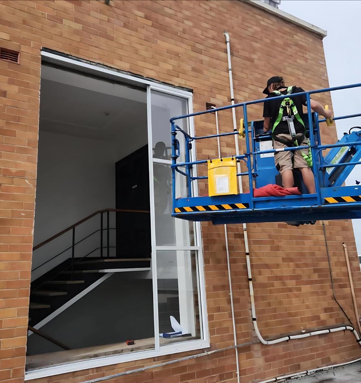 A Man is Standing in a Bucket on Top of a Building — Cessnock Glass in Cessnock, NSW