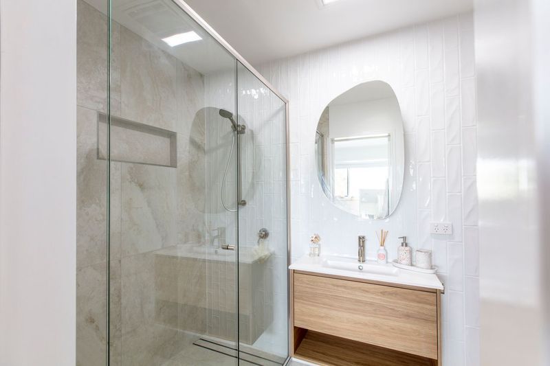 Modern bathroom with glass shower, wooden vanity, and abstract-shaped mirror — Cessnock Glass in Maitland, NSW
