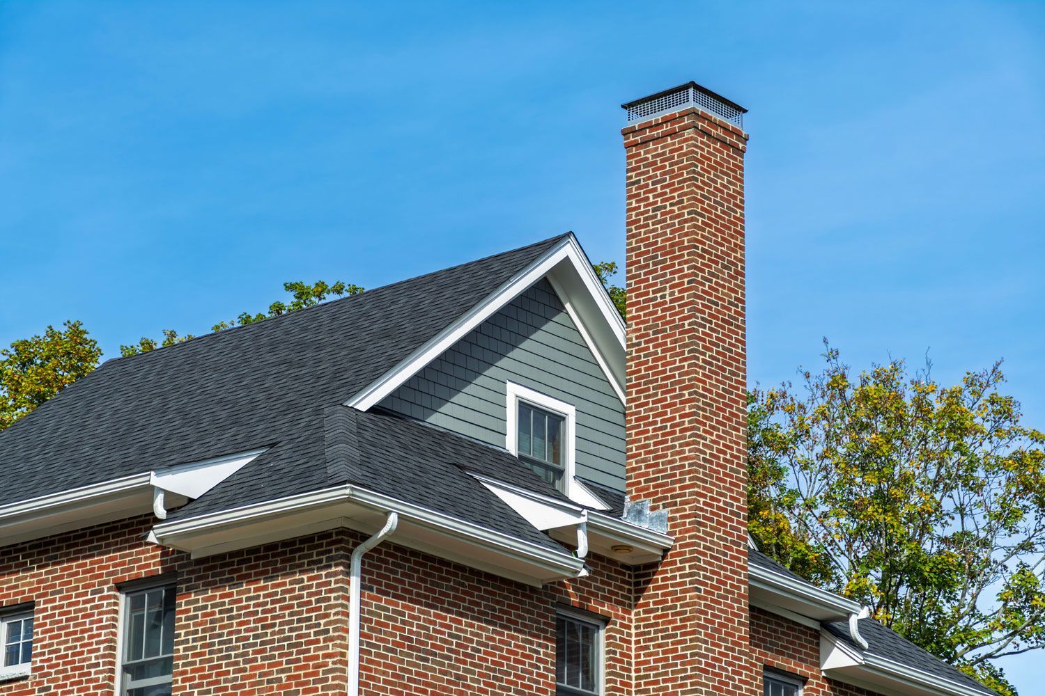 Brick house with gray roof and tall brick chimney against a blue sky Brick house with gray roof and tall brick chimney against a blue sky