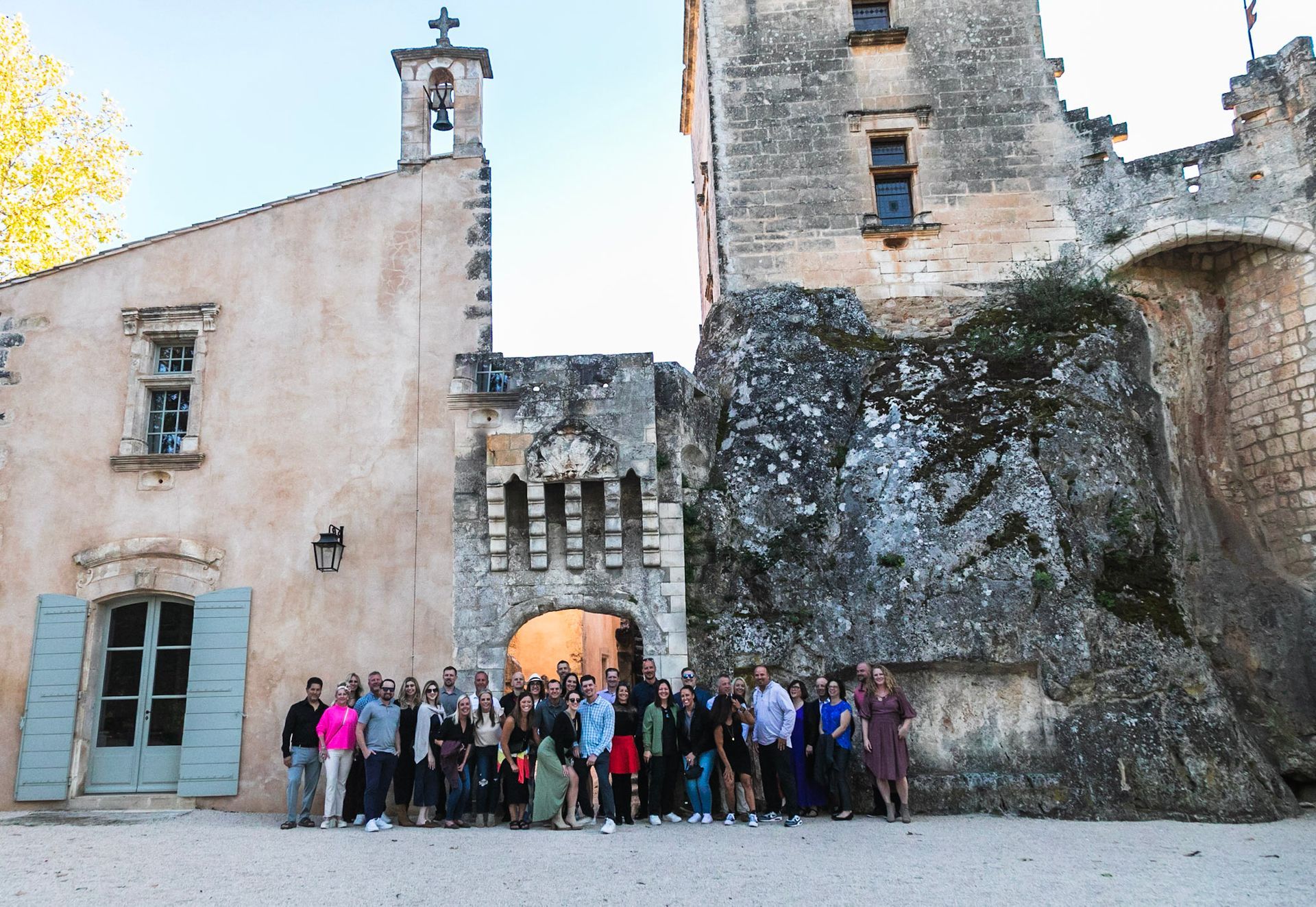 Group of people posing in front of an ancient stone building and a castle under a sunny sky.