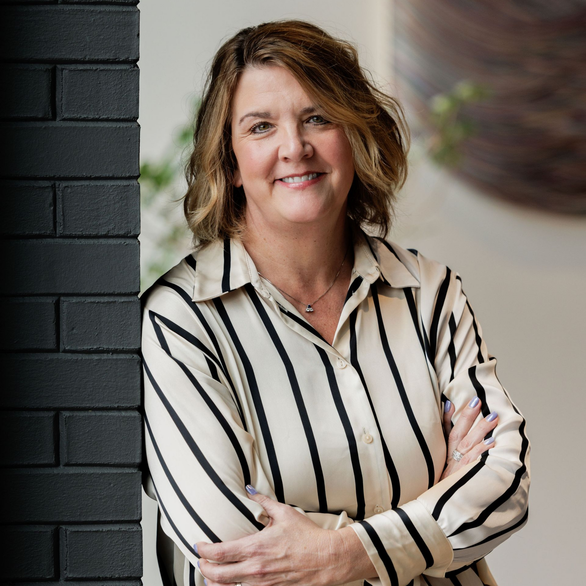 Woman in a striped blouse standing with arms crossed beside a dark brick wall