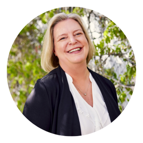 A woman in a blue jacket is smiling with her arms crossed