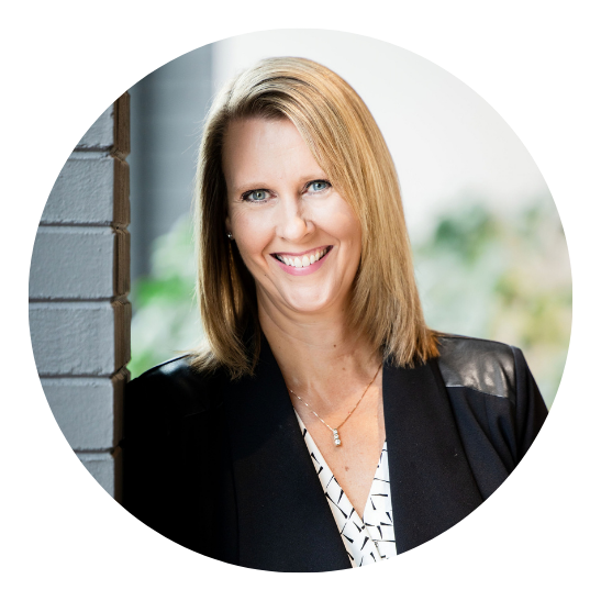 Smiling woman in a black blazer leaning by a brick wall outdoors