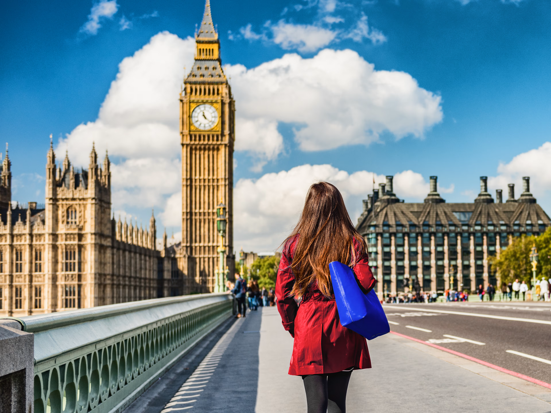 Mulher caminha em direção ao Big Ben em Londres, casaco vermelho, bolsa azul, vista da ponte.