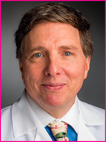 A man in a white coat and tie is smiling for the camera.