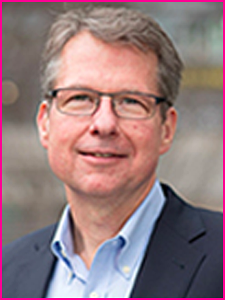 A man wearing glasses and a suit is smiling for the camera.