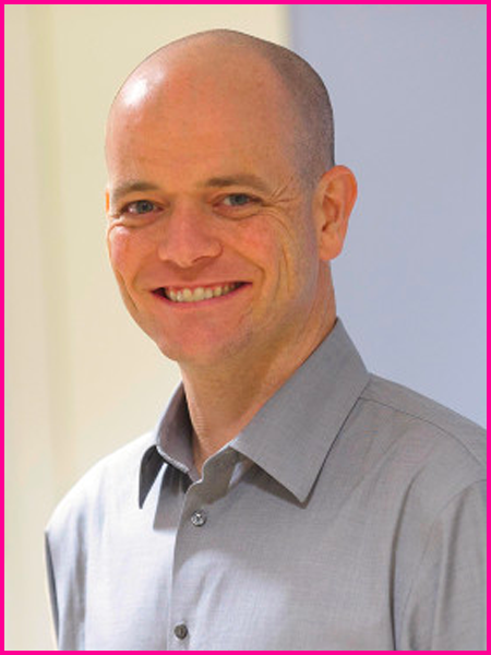 A bald man in a grey shirt is smiling for the camera.