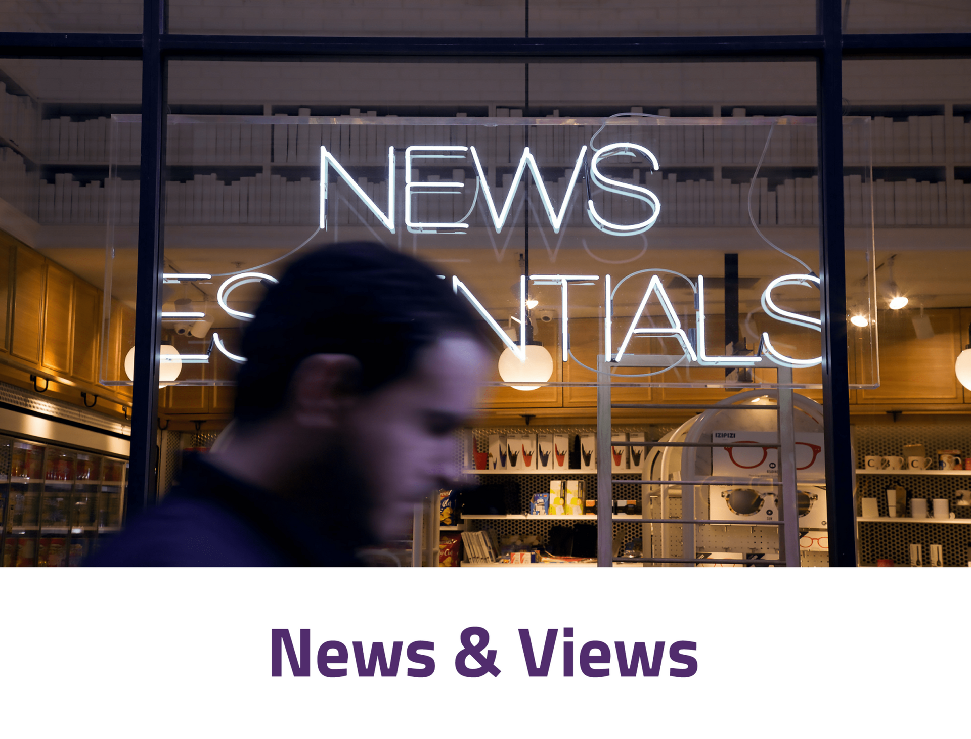 A man is walking in front of a neon sign that says news essentials