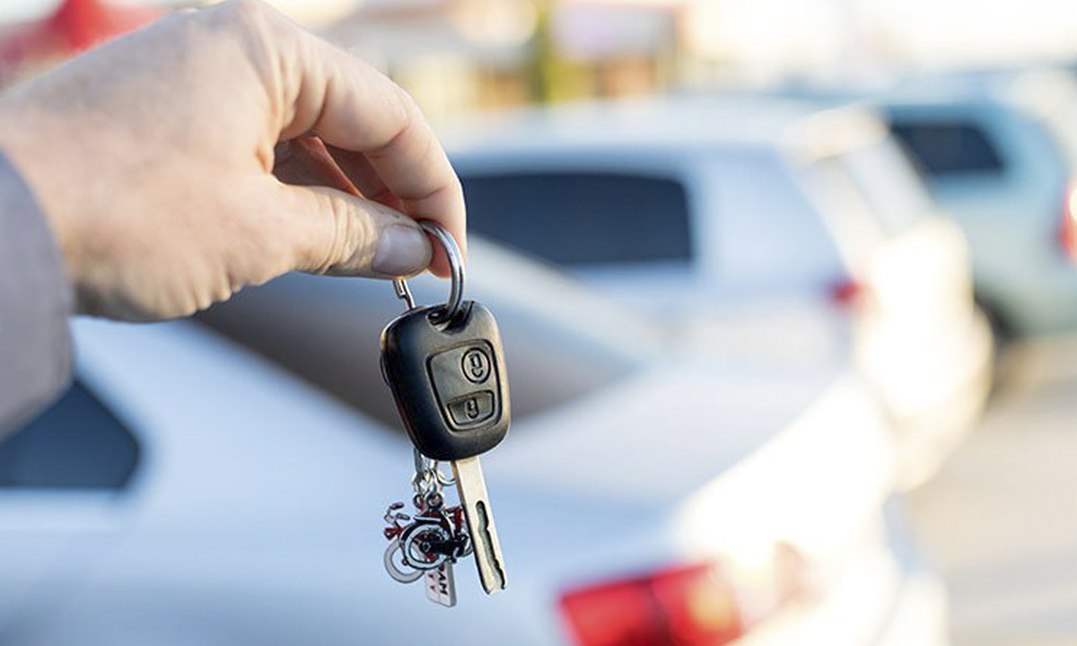 A person is holding a car key in front of a car.