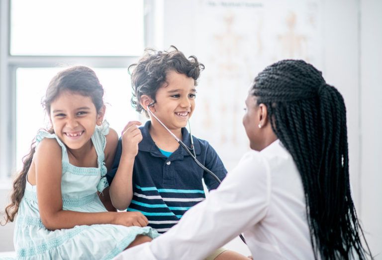 A doctor is listening to a boy and a girl with a stethoscope.