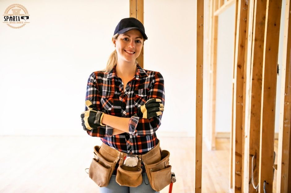A drywall company worker wearing a plaid shirt, a hat, and brown tool belt stands confidently with arms crossed against exposed wooden wall studs in a residential construction site near W Alice Ave, and N 179th Dr, Waddell, AZ.