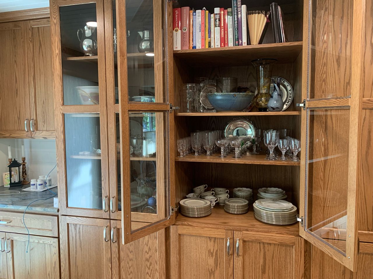 A wooden cabinet filled with plates , bowls , glasses , and books. A wooden cabinet filled with plates , bowls , glasses , and books.