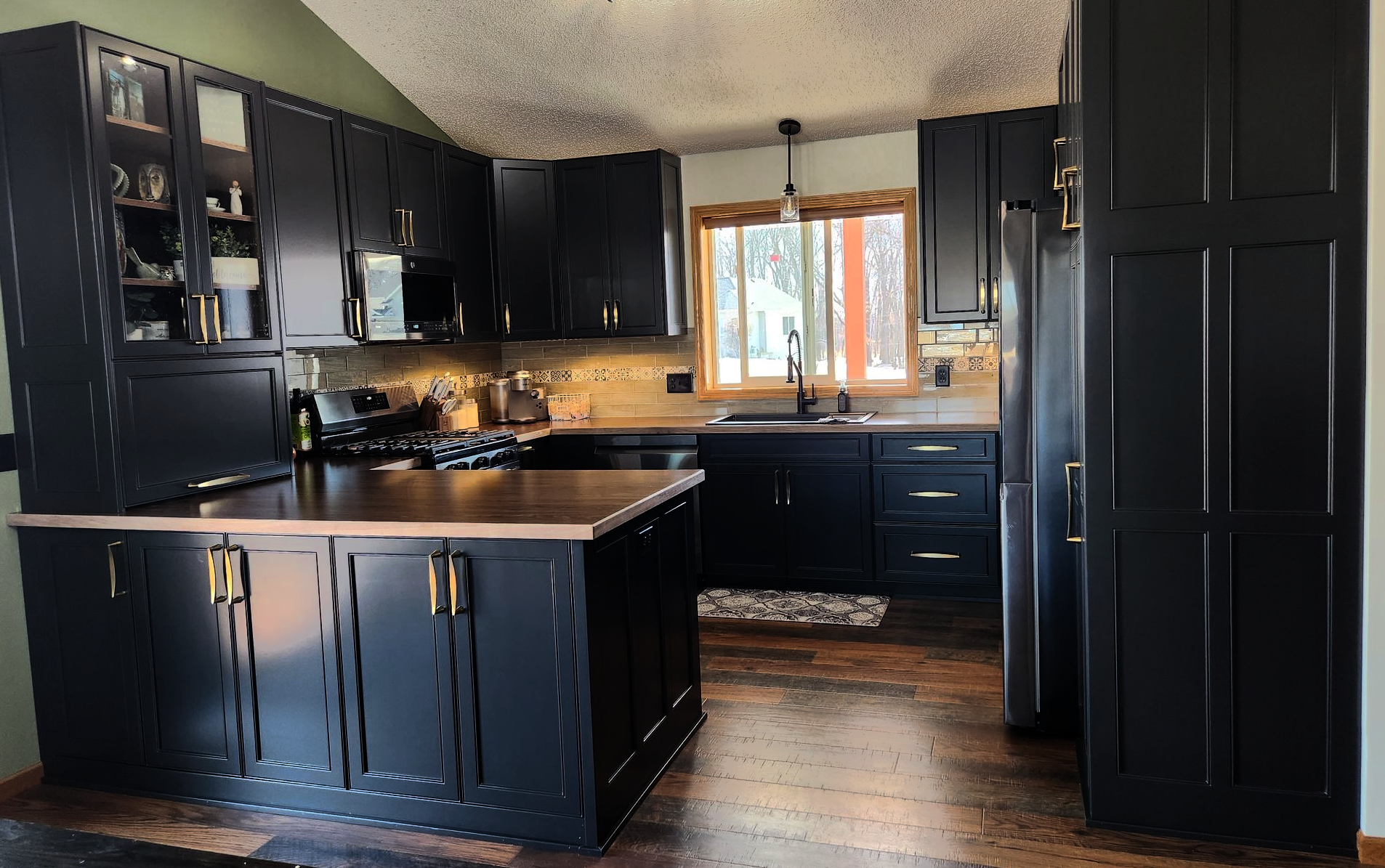 Black painted Casa Collection kitchen cabinetry in East Bethel, Minnesota, with gold hardware and a wood countertop island.