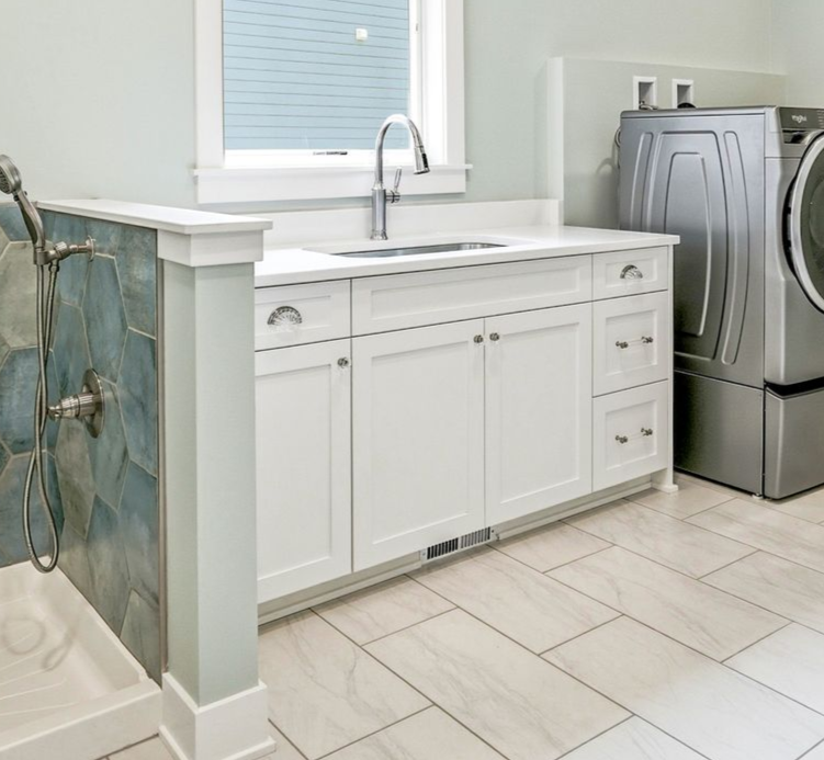 Custom white laundry room cabinetry with utility sink, built-in dog wash station featuring blue hexagon tile, and front-loading washer and dryer in Chisago City, Minnesota.
