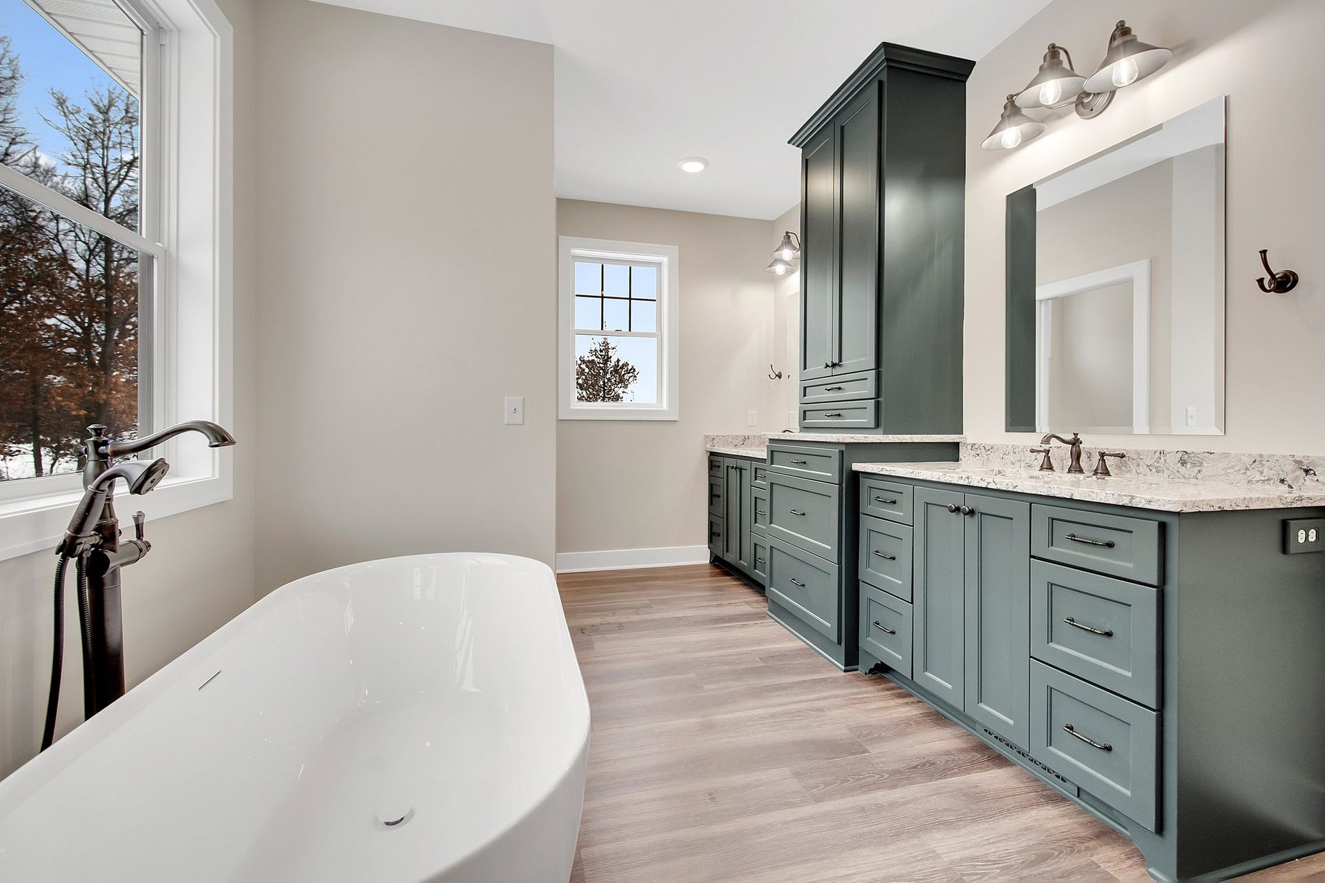 Green painted Casa Collection bathroom cabinetry with double vanity, tall storage cabinet, and freestanding tub.