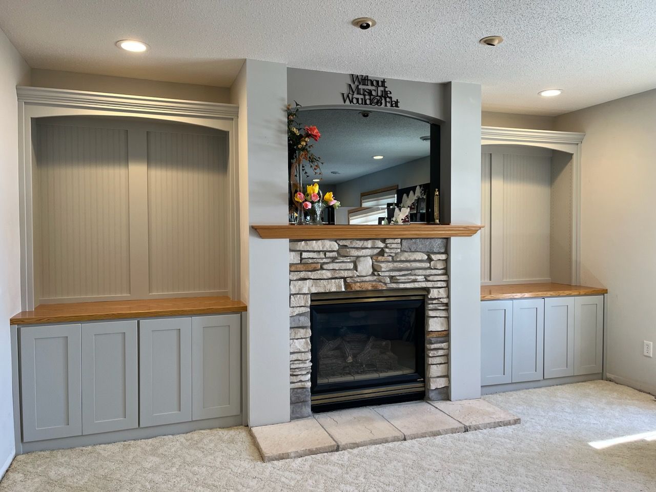 Gray shaker built-in cabinets with oak countertops and arched beadboard niches on both sides of a stone fireplace