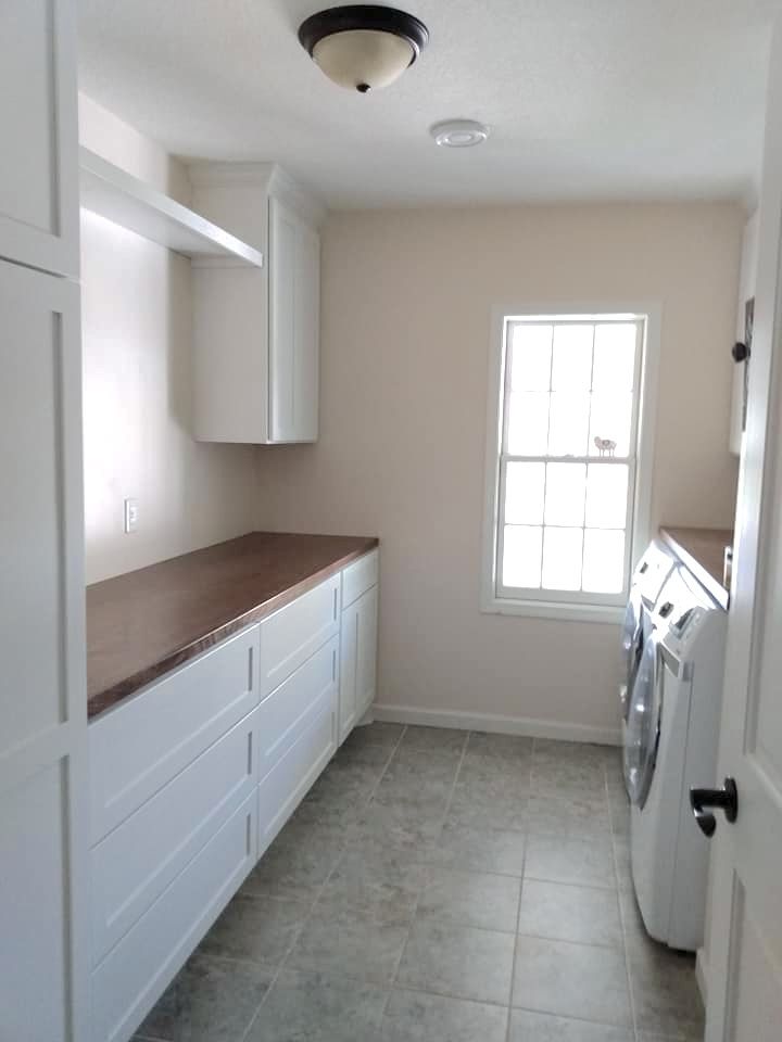 White laundry room cabinetry with a walnut countertop, built-in storage, and space for a washer and dryer.
