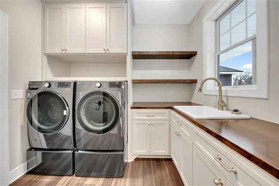 White painted Casa Collection laundry room cabinetry with wood countertops, open shelving, utility sink, and built-in storage.