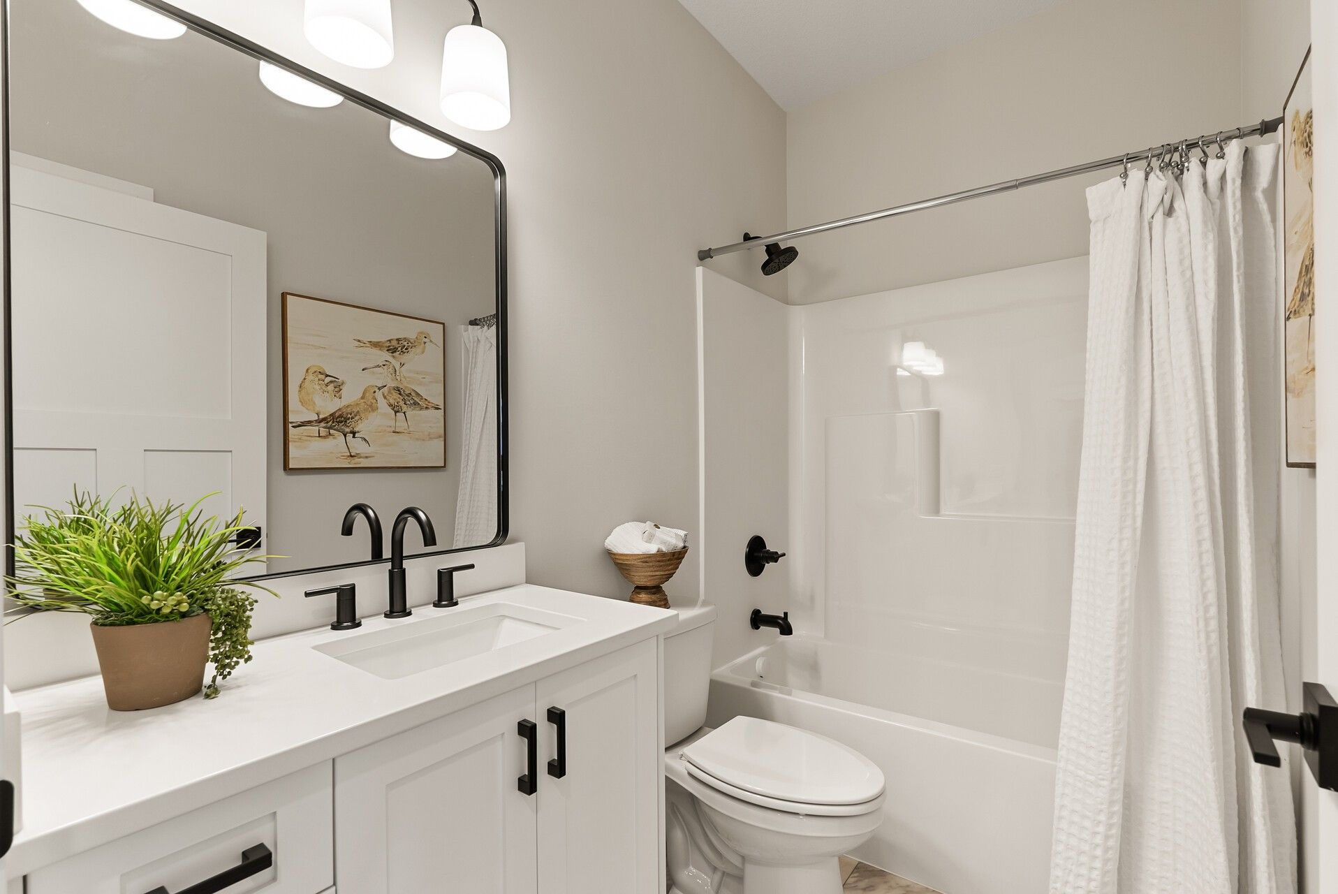 White shaker bathroom vanity in Woodbury, MN with black hardware, white countertop, and tub-shower.