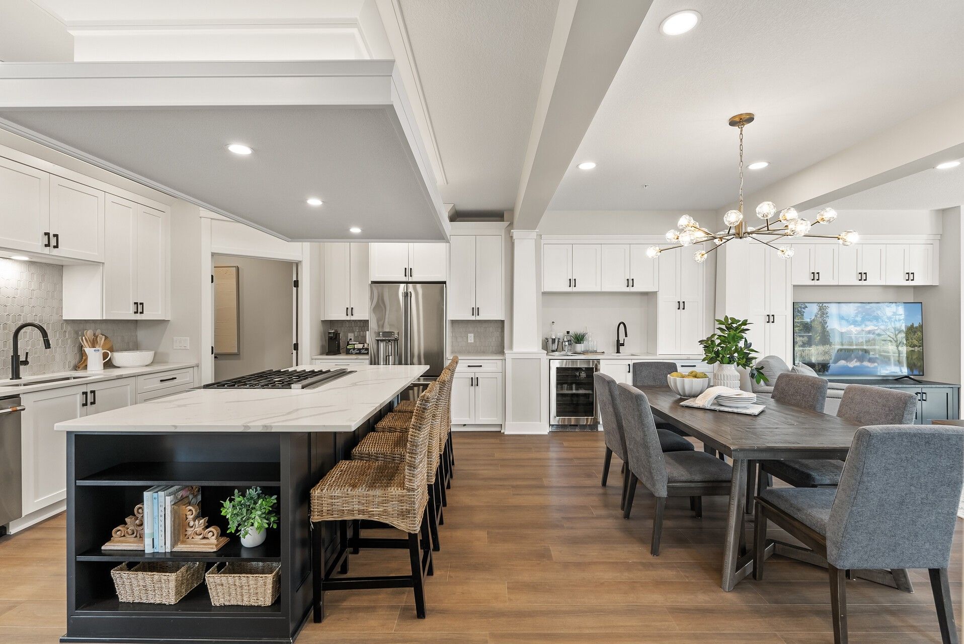 Bright open-concept kitchen with white cabinetry, black island, wood flooring, and adjoining dining 