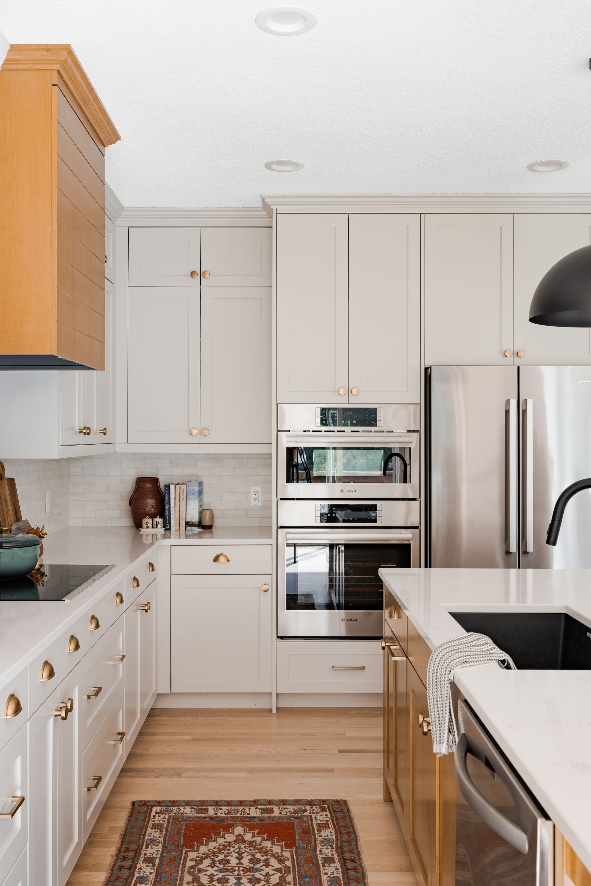 Warm white Signature Collection kitchen cabinetry with natural wood accents, gold hardware, and built-in appliances.