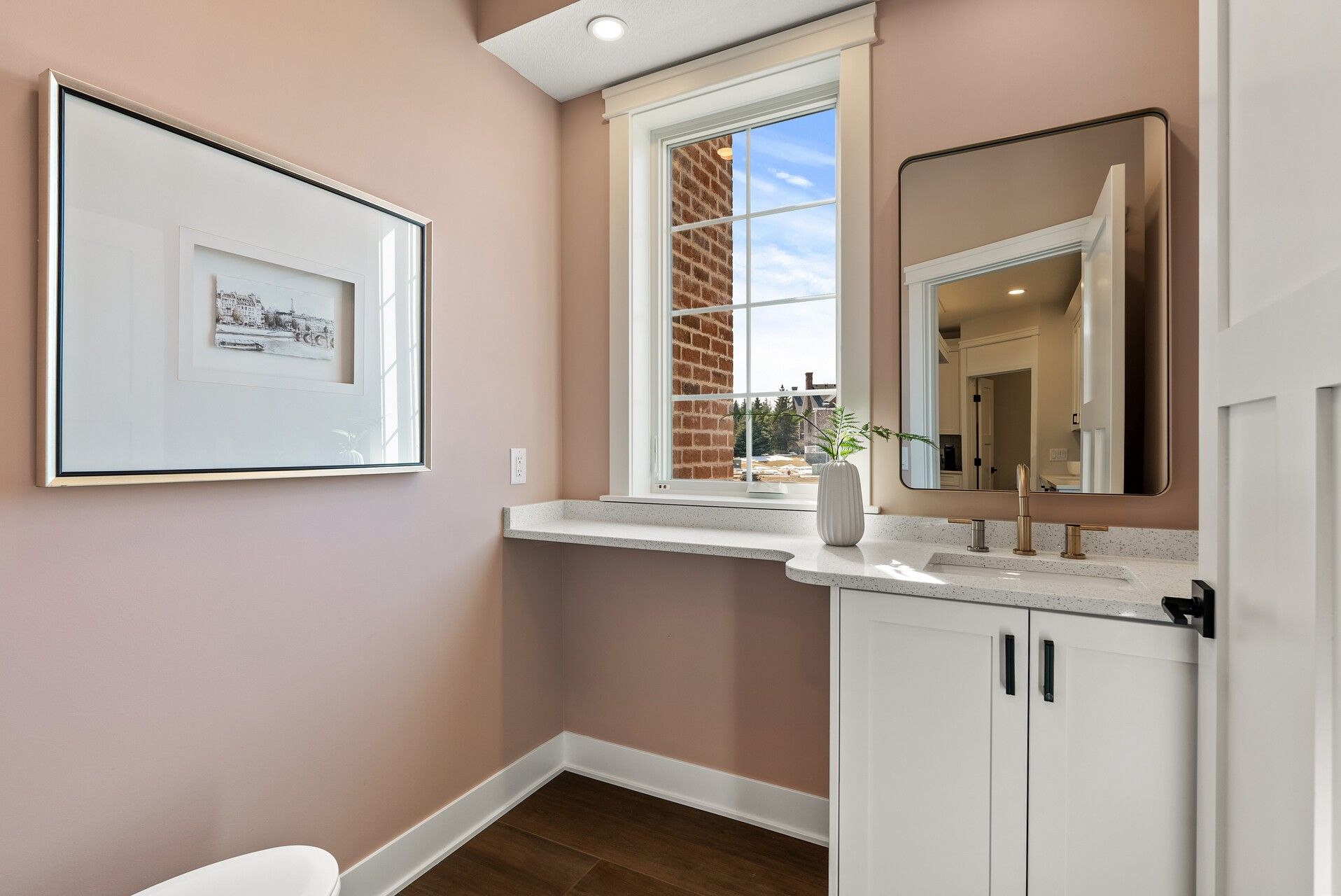 White shaker powder room vanity in Woodbury, MN with black hardware, dark countertop, and warm blush walls.