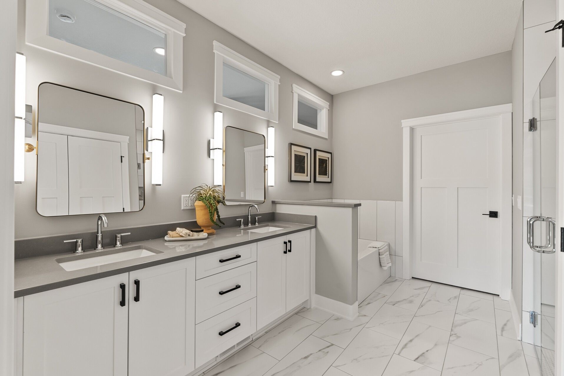 White shaker bathroom vanity in Woodbury, MN with double sinks, dark countertop, black hardware, and upper storage cabinets.
