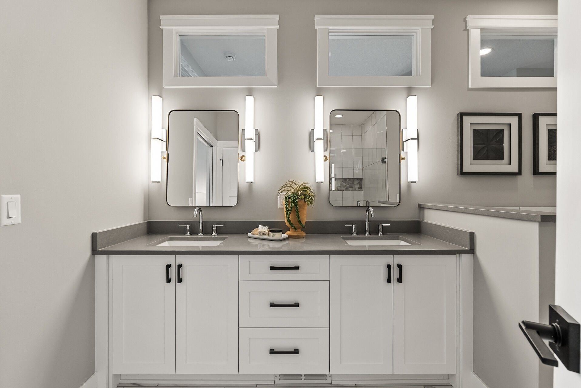 White shaker primary bathroom cabinetry in Woodbury, MN with a long double vanity, dark countertop, and black hardware.