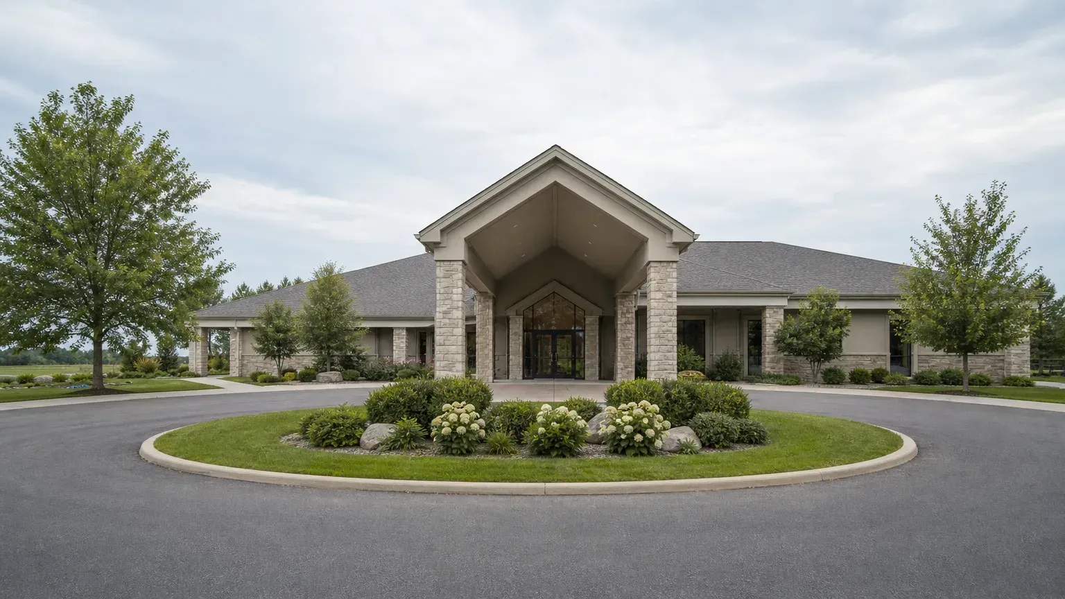 Stone funeral home building in Muskegon, MI, faces a circular drive and flower beds