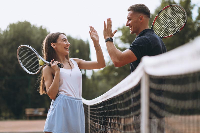 A man and a woman are giving each other a high five on a tennis court.