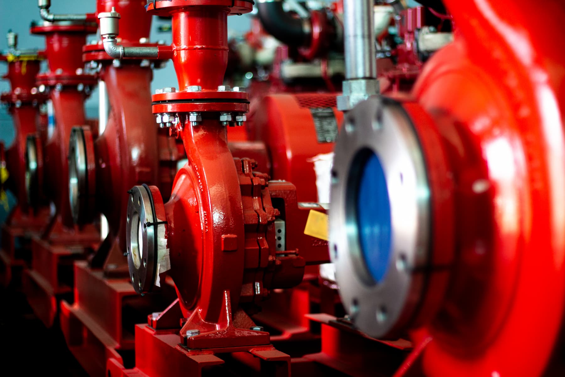 Red industrial fire pumps and pipes in a mechanical room, painted bright red with metal flanges and valves