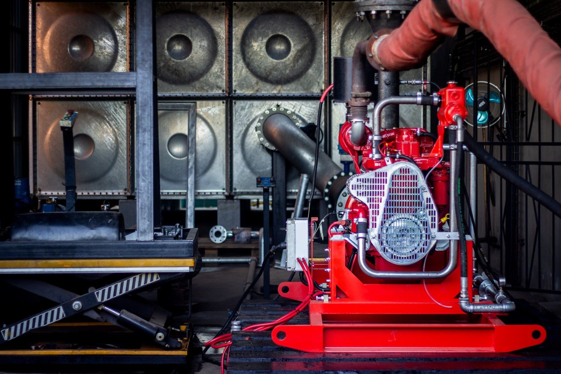 Red industrial generator in a truck bed beside large speaker cabinets, with a person adjusting hoses.