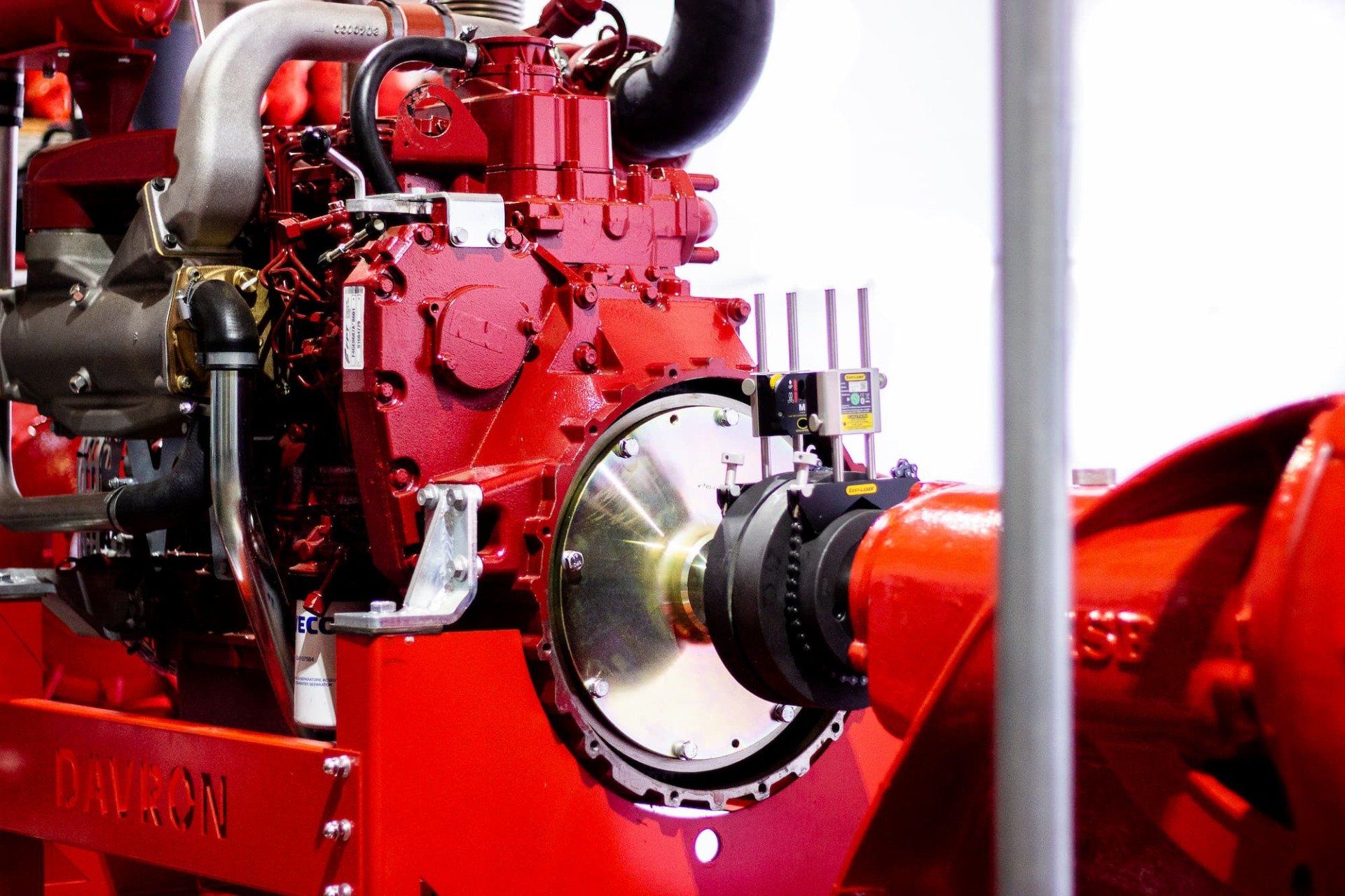 Red industrial engine with metal piping and a bright red coupling in a factory setting