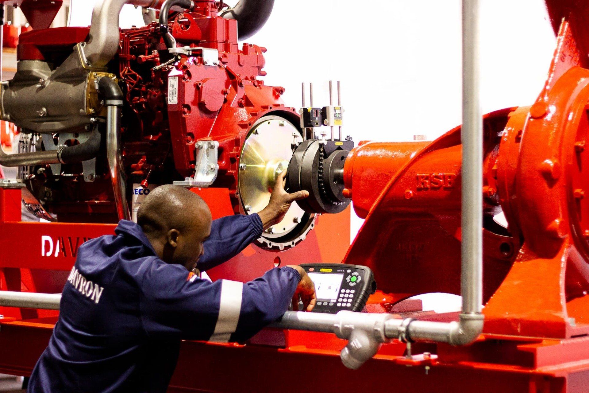 Worker inspecting a large red industrial machine with a wrench in a factory setting