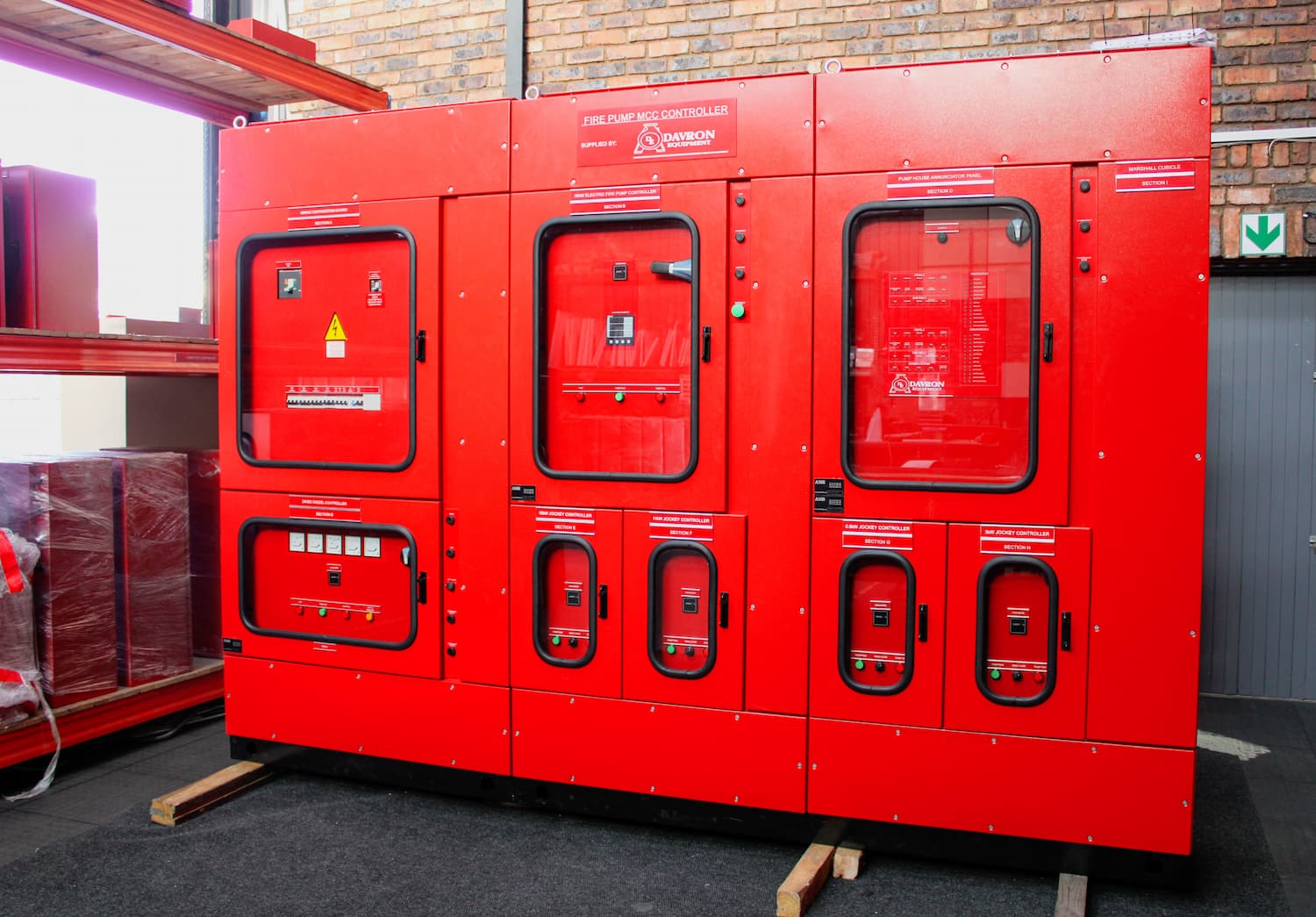 Red industrial fire-safety cabinet with multiple red doors and panels against a brick wall