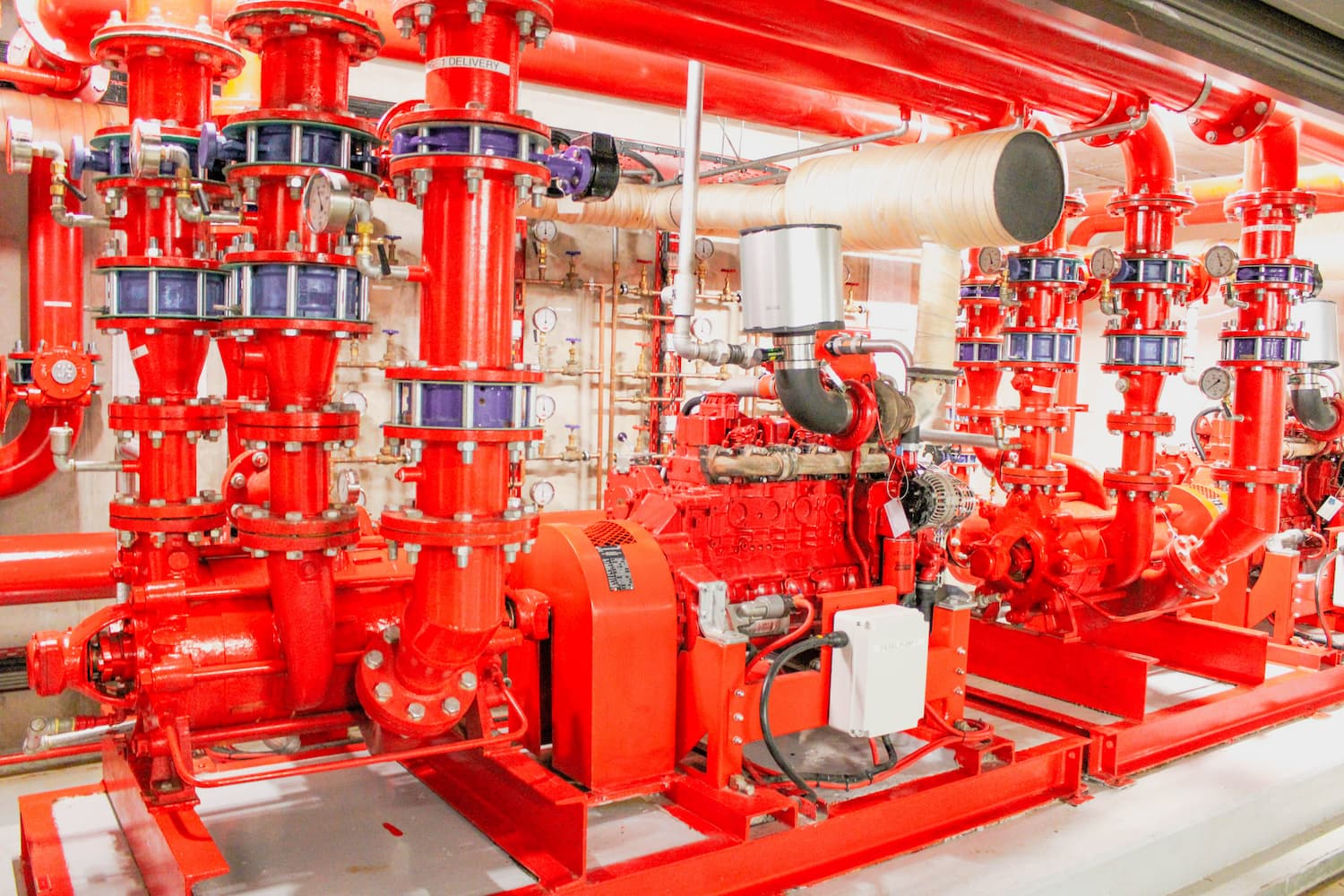 Red industrial pipes and pumps in a mechanical room with bright red fire suppression equipment