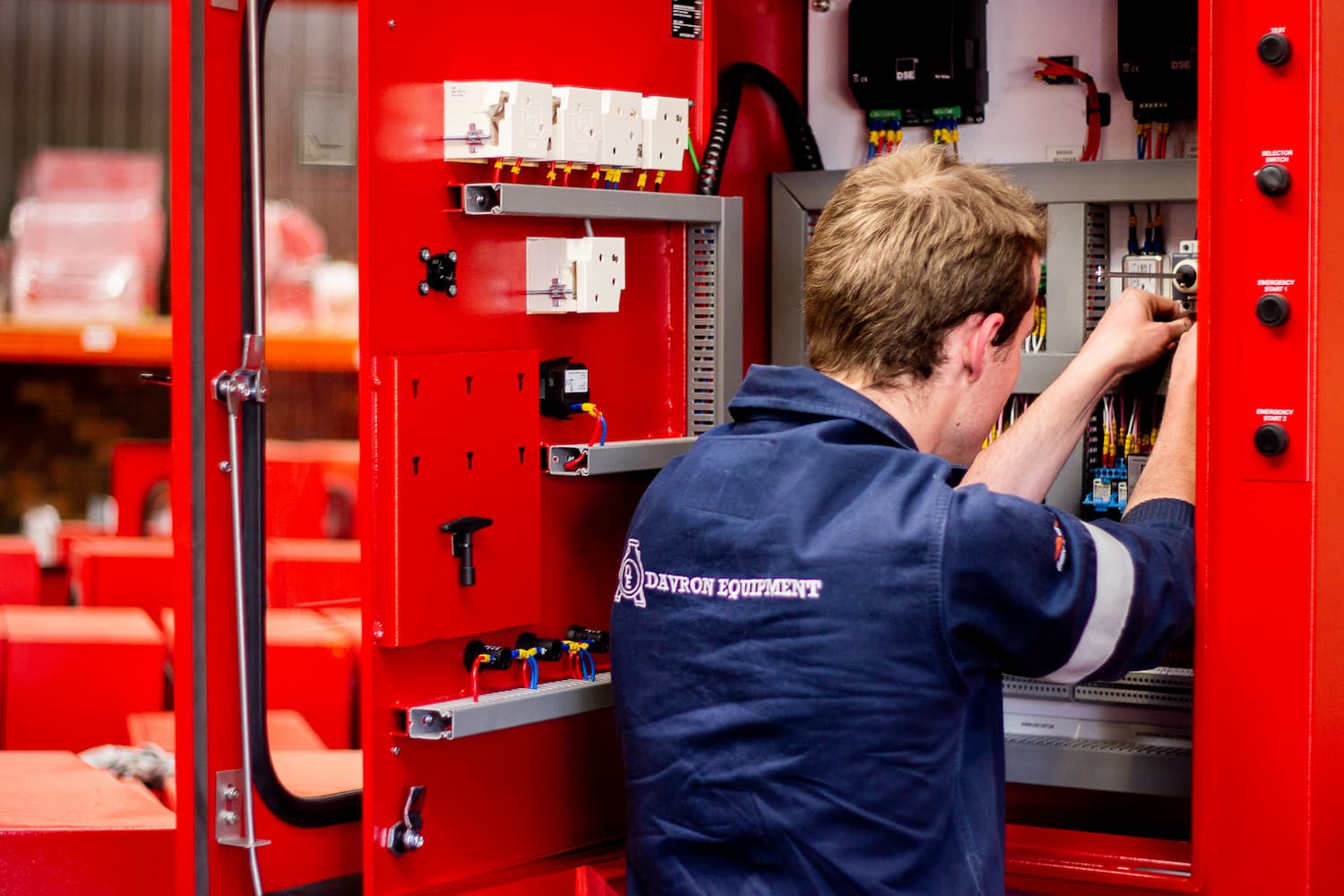 Worker in navy shirt inspecting equipment inside a red industrial machine cabinet