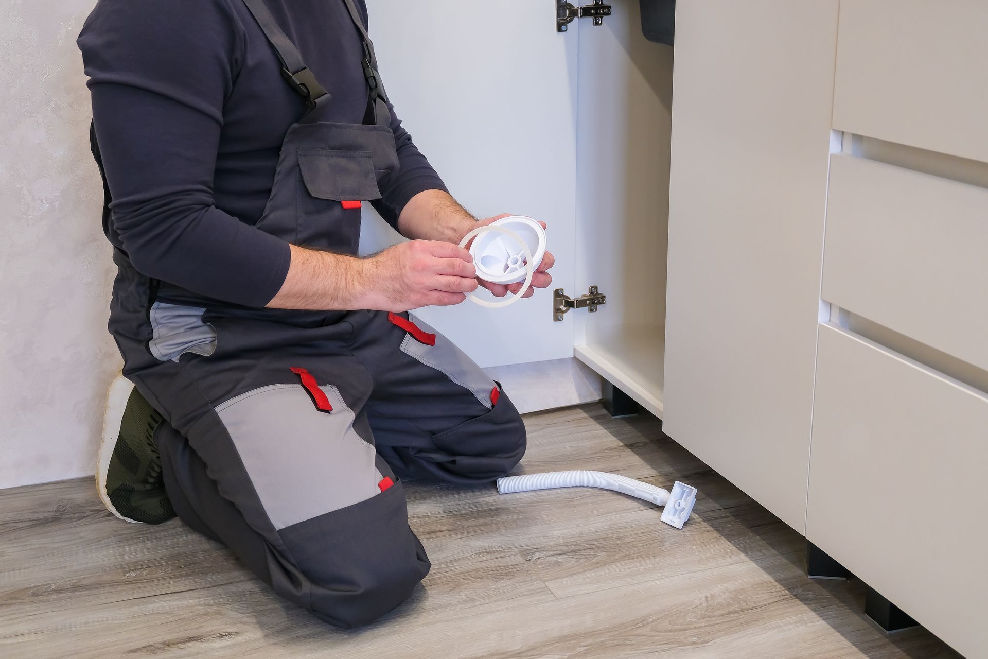Professional plumber installing and repairing a kitchen sink drain pipe under a modern cabinet.