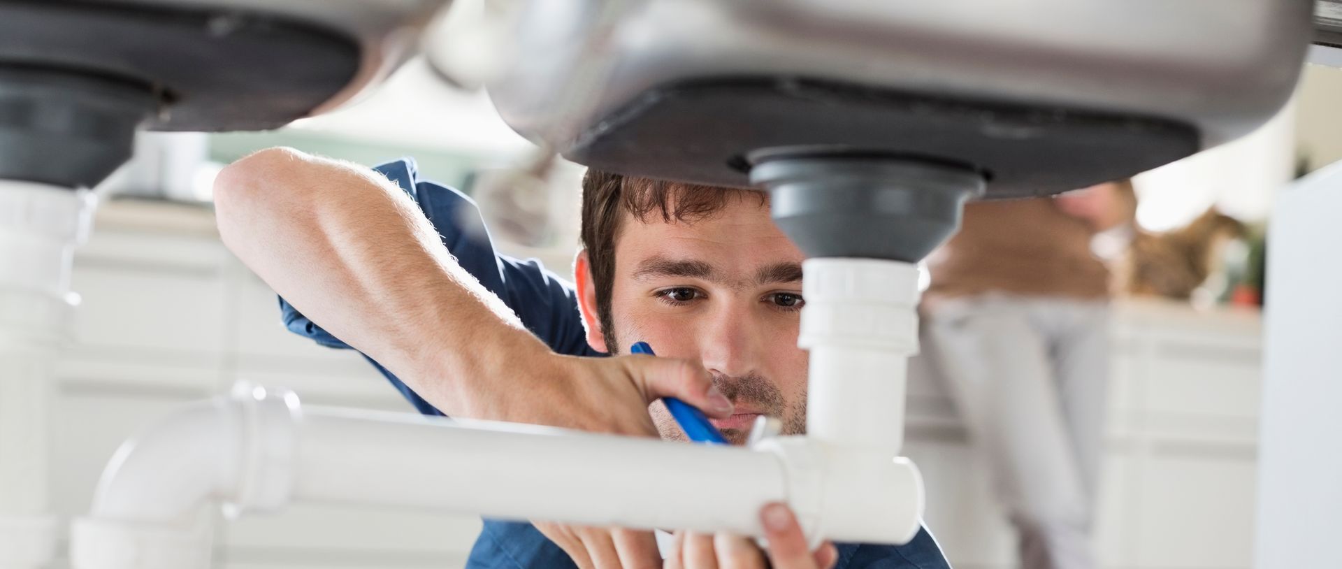 Professional plumber doing a residential plumbing repair on drainpipes under a kitchen sink.