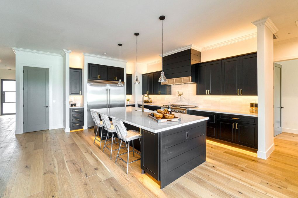 Modern kitchen with black cabinets, white island, pendant lights, and light wood floors