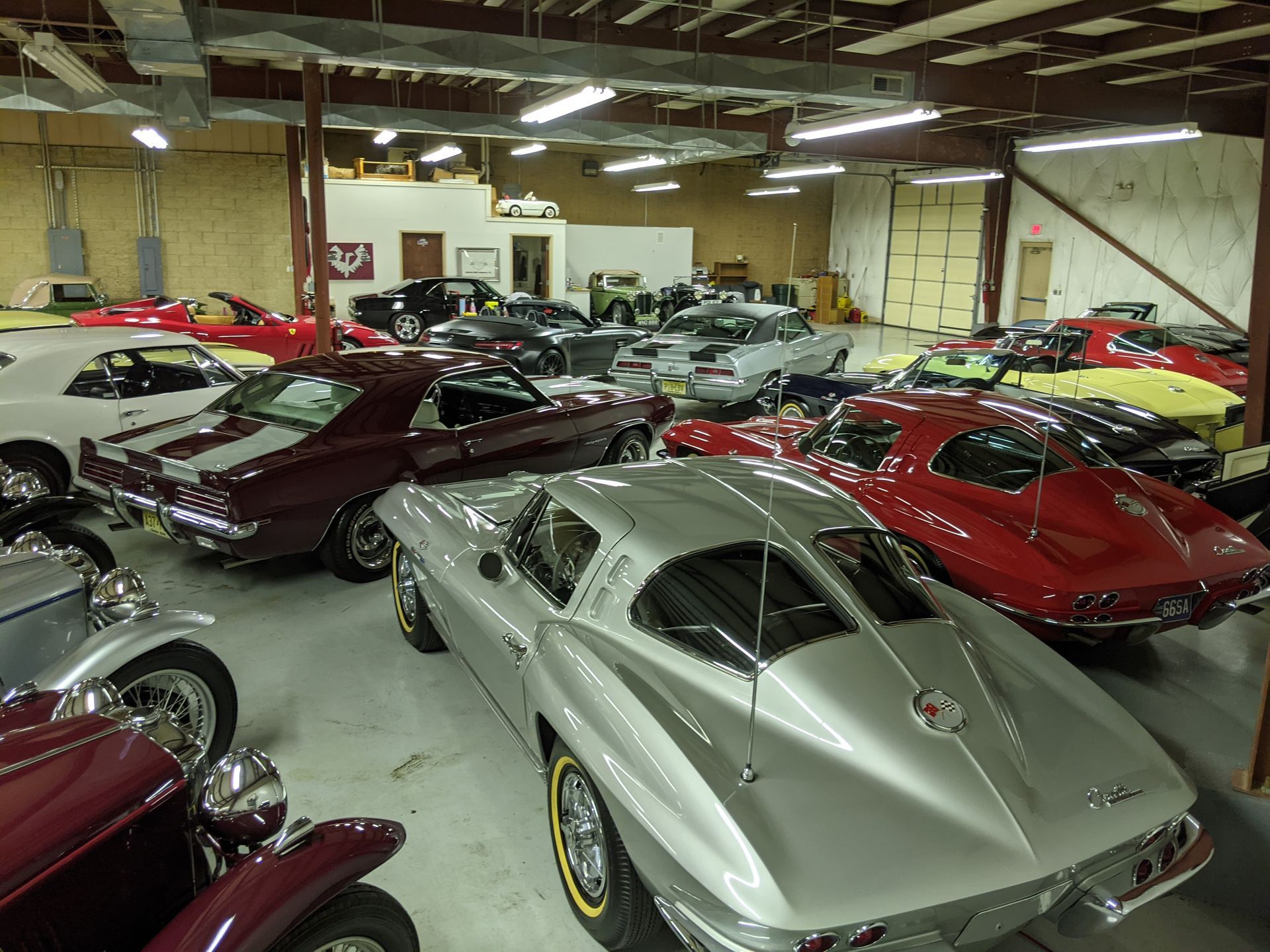Classic sports cars displayed in a showroom, including silver, red, and maroon coupes.