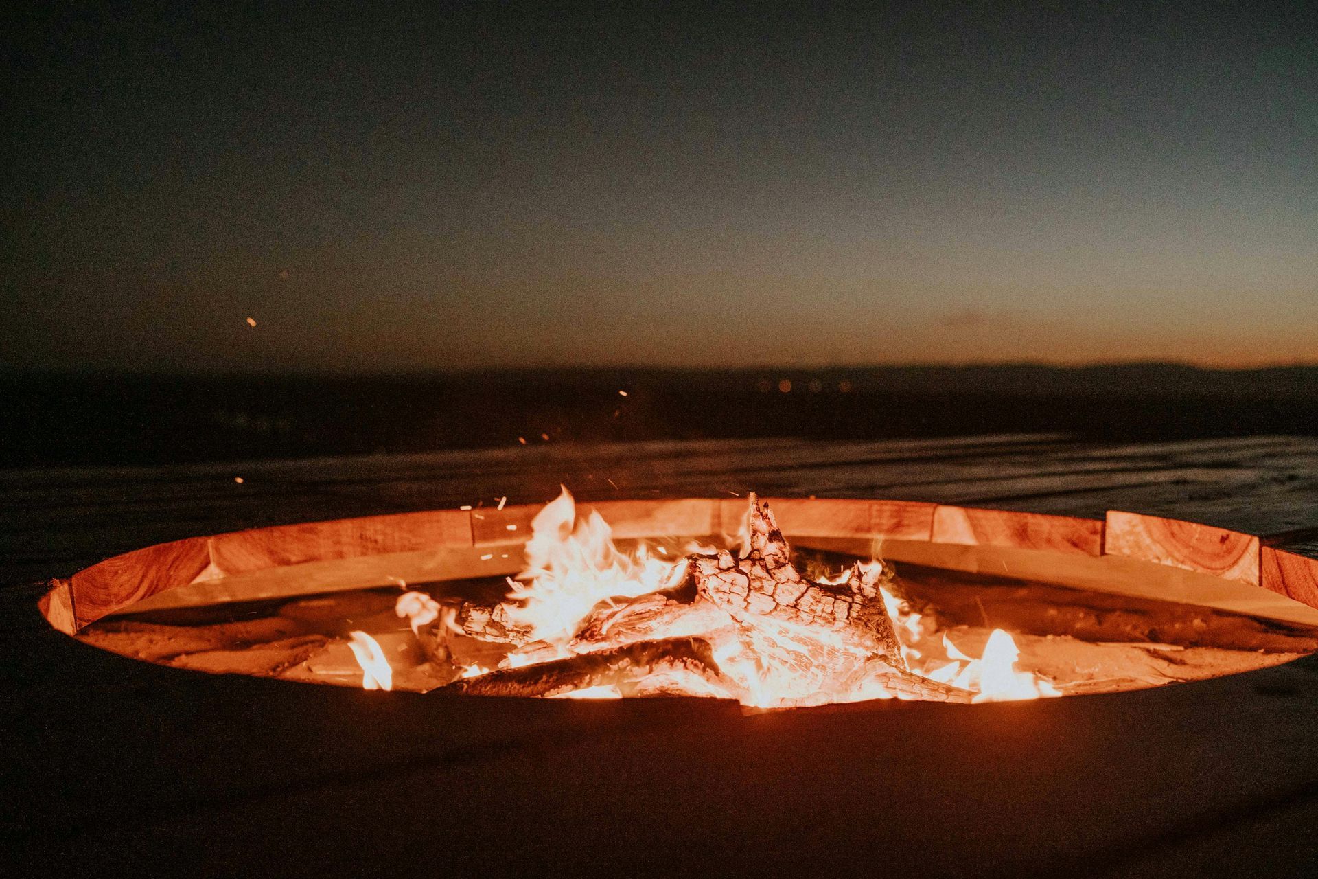 A circular fire pit with bright flames burning at night under a dark sky